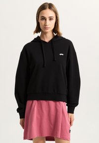 Svart kort hoodie i bomull, med en framficka och dragsko vid huven, kombinerad med en rosa kjol.