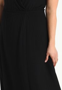 Czarna sukienka z gładkiego, elastycznego materiału. Posiada elastyczny pas i drapowaną konstrukcję, podkreślającą luźny krój.