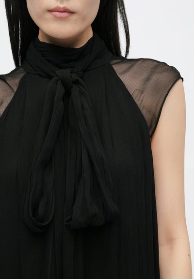 Vestido negro con una textura suave y arrugada, con hombros transparentes y un detalle de bufanda anudada en el escote. Diseño simple y elegante.