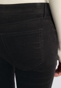 Jeans noirs avec une texture douce, dotés d'une poche arrière, de détails de couture subtils et d'un design ajusté. Le matériau paraît légèrement texturé.