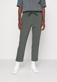 Lätta gröna byxor med elastisk midja och dragsko, med snäva ben och fållade nederkanter. Bärs med vita sneakers.