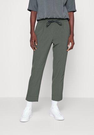 Pantalons verts légers avec une taille élastique et un cordon de serrage, présentant des jambes fuselées et des ourlets à la cheville. Associés à des baskets blanches.