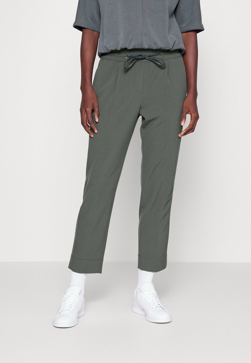 Lätta gröna byxor med elastisk midja och dragsko, med snäva ben och fållade nederkanter. Bärs med vita sneakers.