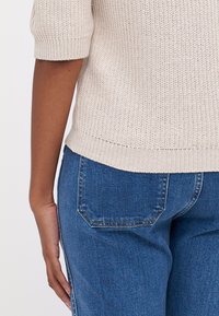 Lys beige strikket genser med korte ermer og ribbete kant, kombinert med mørkeblå denim jeans med klassisk fem-lommersdesign.