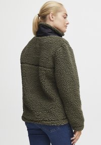 Groene fleecjas met een gestructureerde buitenkant en marineblauwe kraag. Heeft een relaxte pasvorm en zijpanelen voor comfort.