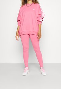 Rosa sweatshirt med vit tre-randig design på ärmarna, kombinerad med matchande rosa leggings. Bärs med vita sneakers. Strukturerad tyg.