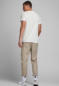 Witte korte mouwen t-shirt, beige linnen broek, witte en grijze sneakers, en witte sokken met zwarte accenten, weergegeven vanuit de achterkant.