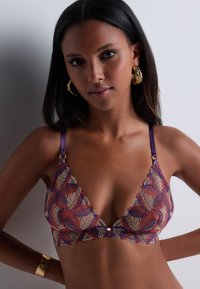 Soutien-gorge triangulaire en dentelle avec des bretelles violettes, comportant des broderies florales rouges et dorées, des bords festonnés et des accents en métal doré.