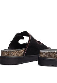 Sandali neri in suede con suola a effetto sughero, dotati di cuciture rosse e dettagli ritagliati sui lati, progettati per il comfort con un tacco spesso.
