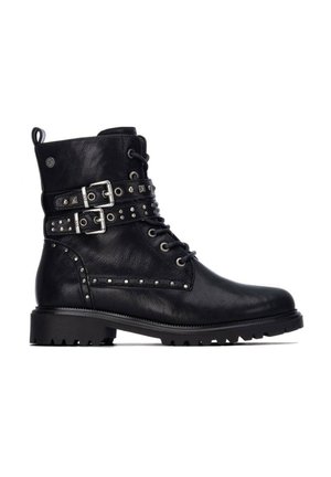 Bota de combate de cuero negro con suela de tacos, correas con doble hebilla, cordones y adornos de tachuelas plateadas a lo largo de los lados y las correas.