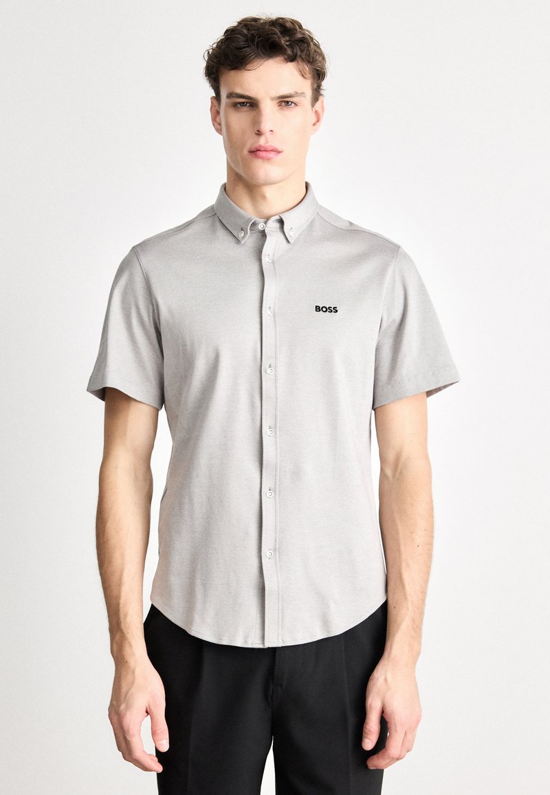 Koszula z krótkim rękawem na guziki w jasnoszarym materiale o gładkiej fakturze. Na piersi znajduje się czarne logo „BOSS”.