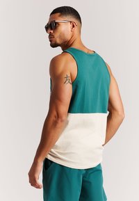 Top sin mangas con bloques de color en tonos azul verdoso y crema, con un ajuste relajado. Ligero, de textura suave, cuello redondeado y sin cierres visibles.