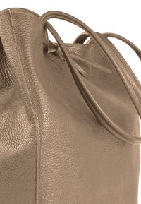 Grote taupekleurige leren tas met een gestructureerd oppervlak, voorzien van twee lange hengsels en een open bovenkant, met zichtbare stiksels en een samengeknepen ontwerp.