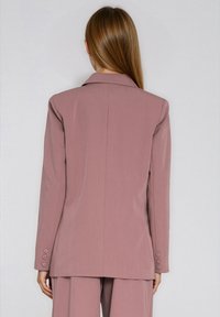 Różowy dopasowany żakiet z klapami z wycięciem, długimi rękawami i mankietami na guziki. Gładki materiał o usztywnionym kroju i gładkim, jednolitym tyle.