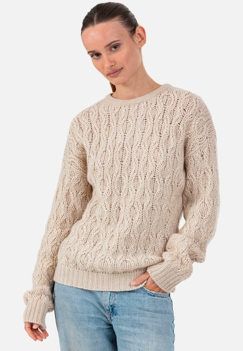 Pull beige en maille avec un motif ondulé texturé, col rond et poignets côtelés. Associé à un jean bleu clair pour un look décontracté.