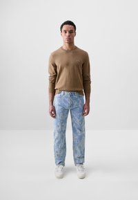 Suéter de punto marrón, jeans de camuflaje azul y zapatillas blancas. Diseño minimalista con un logo en el suéter.