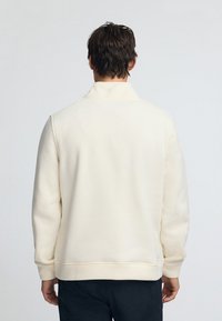 Sudadera de forro polar color crema claro con cuello alto, puños y dobladillo acanalados. Diseño simple, textura suave y corte relajado.