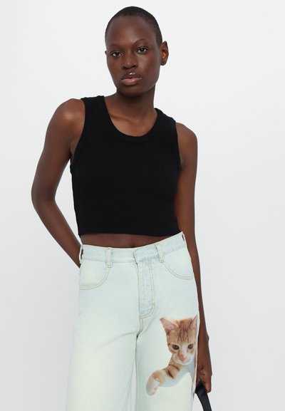 Zwarte geribbelde crop top met een ronde halslijn, gecombineerd met lichtblauwe jeans met een geprinte oranje tabby kat op de rechterdij.
