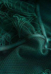 Tamnozeleni �čipkasti materijal s složenim cvjetnim uzorcima, složen s teksturiranom mrežastom podlogom. Glatka obruba naglašava rubove.