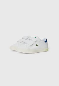 Ténis brancos com duas tiras de velcro, parte superior em couro, calcanhar azul contrastante, detalhe verde na língua e sola de borracha texturizada.