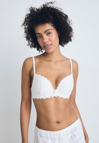 Soutien-gorge en dentelle blanche avec des bords festonnés, présentant des motifs floraux et des bretelles fines ajustables. Tissu léger, conçu pour le confort et l'ajustement.