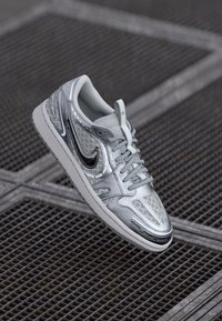 Scarpe da ginnastica argento con finitura lucida, pannelli in rete stampata e logo Swoosh nero. Design con lacci, punta arrotondata e suola testurizzata.