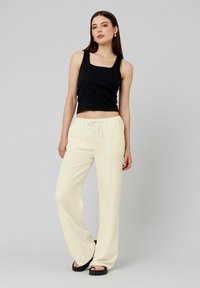 Top court noir à côtes associé à un pantalon large beige clair avec taille élastique et cordon de serrage. Texture lisse ; design décontracté.