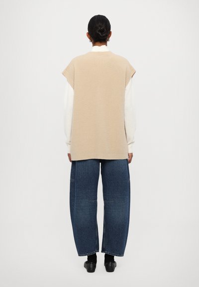 Beige strikket ærmeløs sweater med ribbet tekstur, parret med løse mørkeblå denimbukser. Sættet har diskrete skræddersyede detaljer.