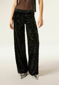 Zwarte pailletten broek met een wijde pijpen ontwerp, voorzien van een glanzende textuur en glimmende pailletten, gecombineerd met metallic puntige schoenen.