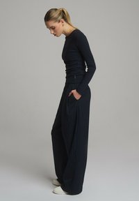 Granatowa bluzka z długim rękawem i szerokie spodnie w paski. Bluzka jest dopasowana; spodnie są luźne, z kieszeniami i fałdami. Białe trampki dopełniają całość.