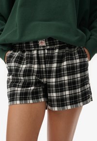 Zwart-witte geruite korte broek met een elastische tailleband en een label aan de achterkant. Zachte stof en een casual ontwerp.