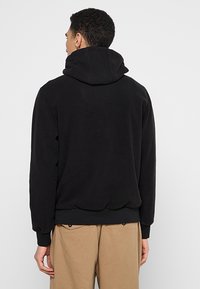 Schwarzer Fleece-Pullover mit großer, verstellbarer Kapuze und gerippten Bündchen. Der Stoff wirkt weich und hat eine glatte Textur.