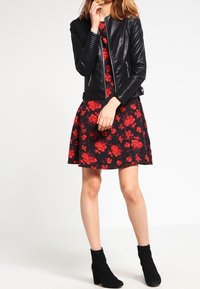 Czarna motocyklowa kurtka z sztucznej skóry z pikowanymi akcentami, połączona z czarną sukienką do kolan z czerwonym kwiatowym nadrukiem. Czarne botki do kostki.