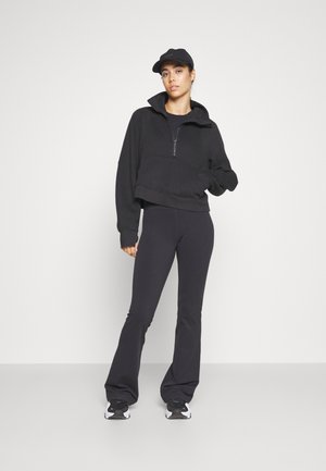 Black cropped hoodie with high collar and half zip, paired with black flared pants. Black cap and athletic shoes complete the look.