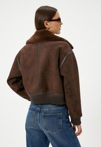 Bruine suède jas met een nep bontkraag, geribbelde zoom, leren accenten en een cropped ontwerp, gecombineerd met hoge taille blauwe jeans.
