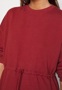 Sweat-shirt rouge en coton avec un col rond, une coupe ample et un cordon élastique à la taille. Texture douce et détails minimalistes.