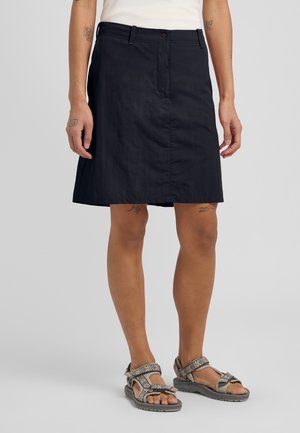 Marineblauwe knie-lange rok met een rits en knoopsluiting aan de voorkant, gemaakt van een gladde stof, gecombineerd met gezandstraalde sandalen met verstelbare banden.
