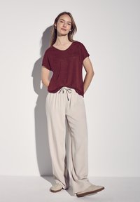 Maroniefarvet kortærmet top parret med lysebeige vidde-bukser. Outfittet har en snøre i taljen og lyse, afslappede sko.