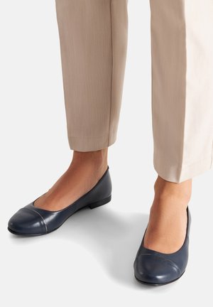 Bailarinas azul marino con punta redondeada y detalle de costura contrastante. Material de cuero liso y tacón bajo cuadrado, combinadas con pantalones beige.