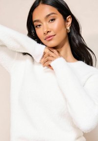 Weißer, flauschiger Pullover mit Rundhalsausschnitt und langen Ärmeln, ausgestattet mit gerippten Bündchen. Sanfte Textur mit lockerer Passform.