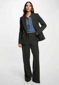 Blazer grigio a quadri su misura con doppi bottoni, abbinato a una camicia di jeans blu. L'outfit include pantaloni a gamba ampia e scarpe nere.