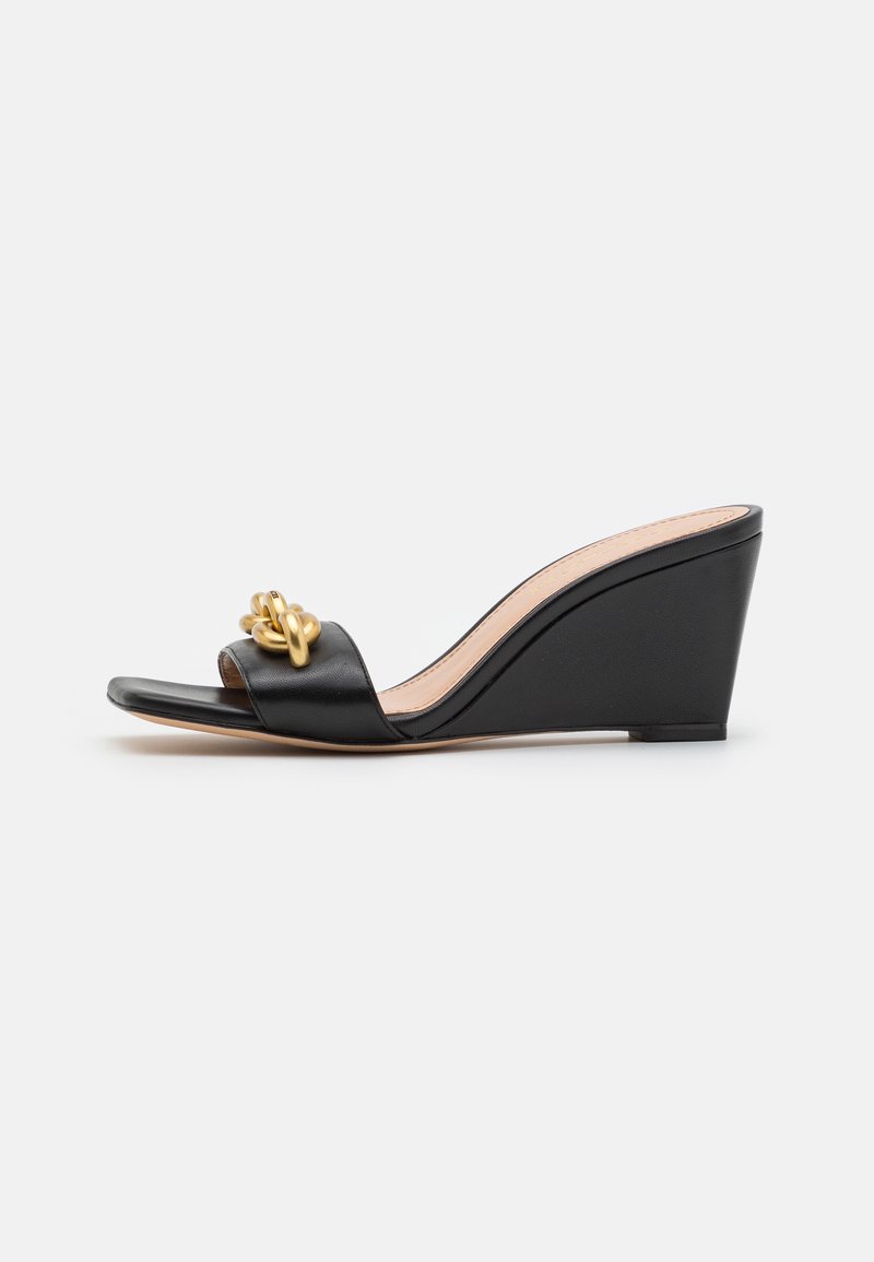 Sandale compensée noire en cuir lisse, dotée d'une large bride et d'un nœud décoratif en métal doré à l'avant. Talon compensé texturé.