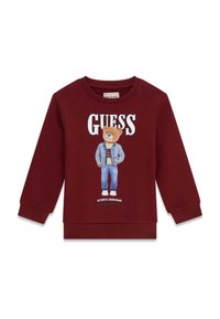 Sweat-shirt bordeaux avec un motif d'ours en tenue en jean. Logo "GUESS" au-dessus, poignets côtelés et texture de tissu douce.