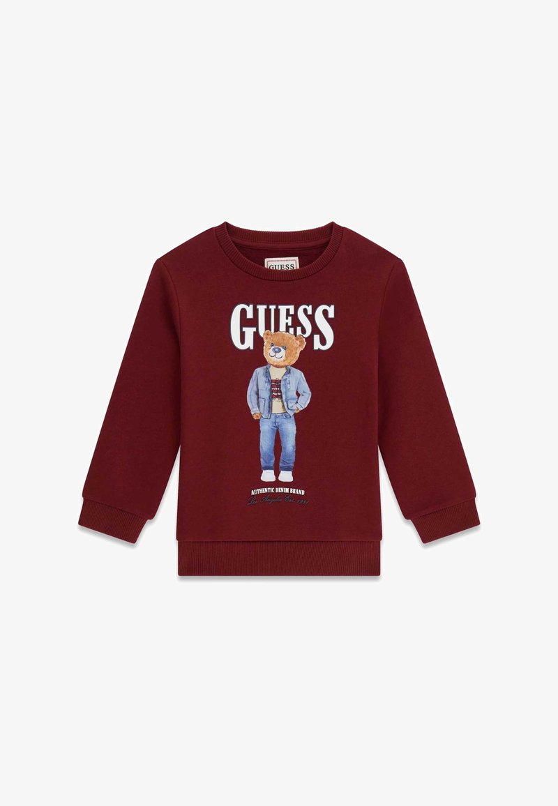 Sweat-shirt bordeaux avec un motif d'ours en tenue en jean. Logo "GUESS" au-dessus, poignets côtelés et texture de tissu douce.