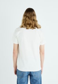 Kortærmet hvid t-shirt lavet af bomuld, med en rund halsudskæring og en afslappet pasform, vist fra ryggen med en glat tekstur.