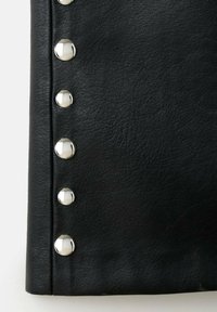 Tissu en cuir noir avec une texture lisse, comportant trois clous métalliques argentés le long du bord, mettant en avant un détail de design moderne.