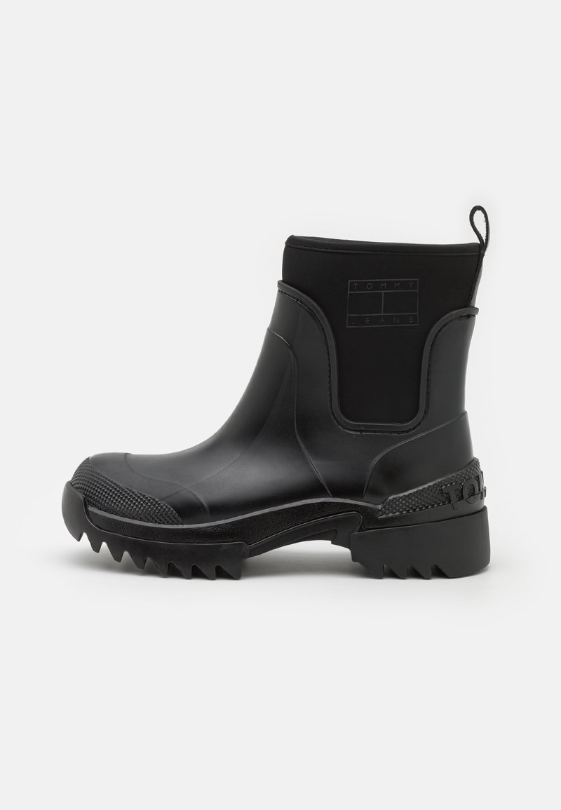 Botte cheville noire imperméable avec une semelle en caoutchouc texturée, au design élégant, à talon haut, et avec un logo sur le côté et à l'arrière.