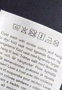L’étiquette de lavage indique : laver à 40°C, ne pas utiliser d'eau de Javel, ne pas sécher en machine, repasser à basse température, ne pas nettoyer à sec, plus instructions d’entretien en plusieurs langues.