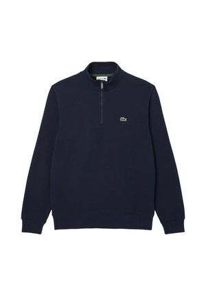 Felpa blu navy con zip a quarto, caratterizzata da maniche lunghe e un piccolo logo verde Lacoste sul lato sinistro del petto. Texture morbida e colore solido.
