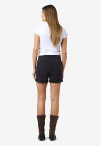 Juodi džinsiniai šortai su aukštu liemeniu, apvyniotais kraštais ir užpakalinėmis kišenėmis. Suderinti su prigludusia balta marškinėliais ir rudos spalvos iki kelių botais.